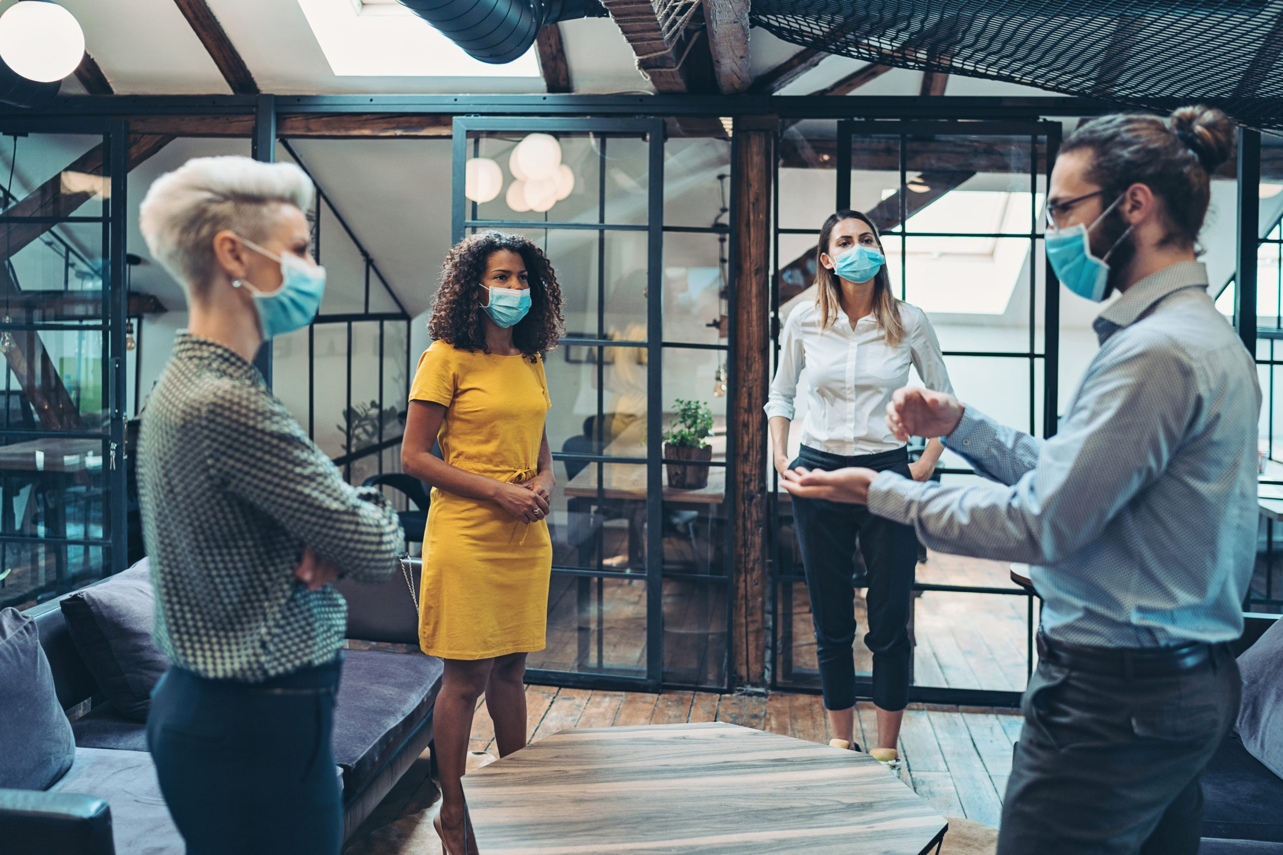 Group of entrepreneurs wearing masks and standing at a distance Business persons with protective masks meet in a co-working area