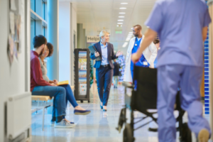 A businesswoman walks through a busy hospital hallway talking to a doctor.